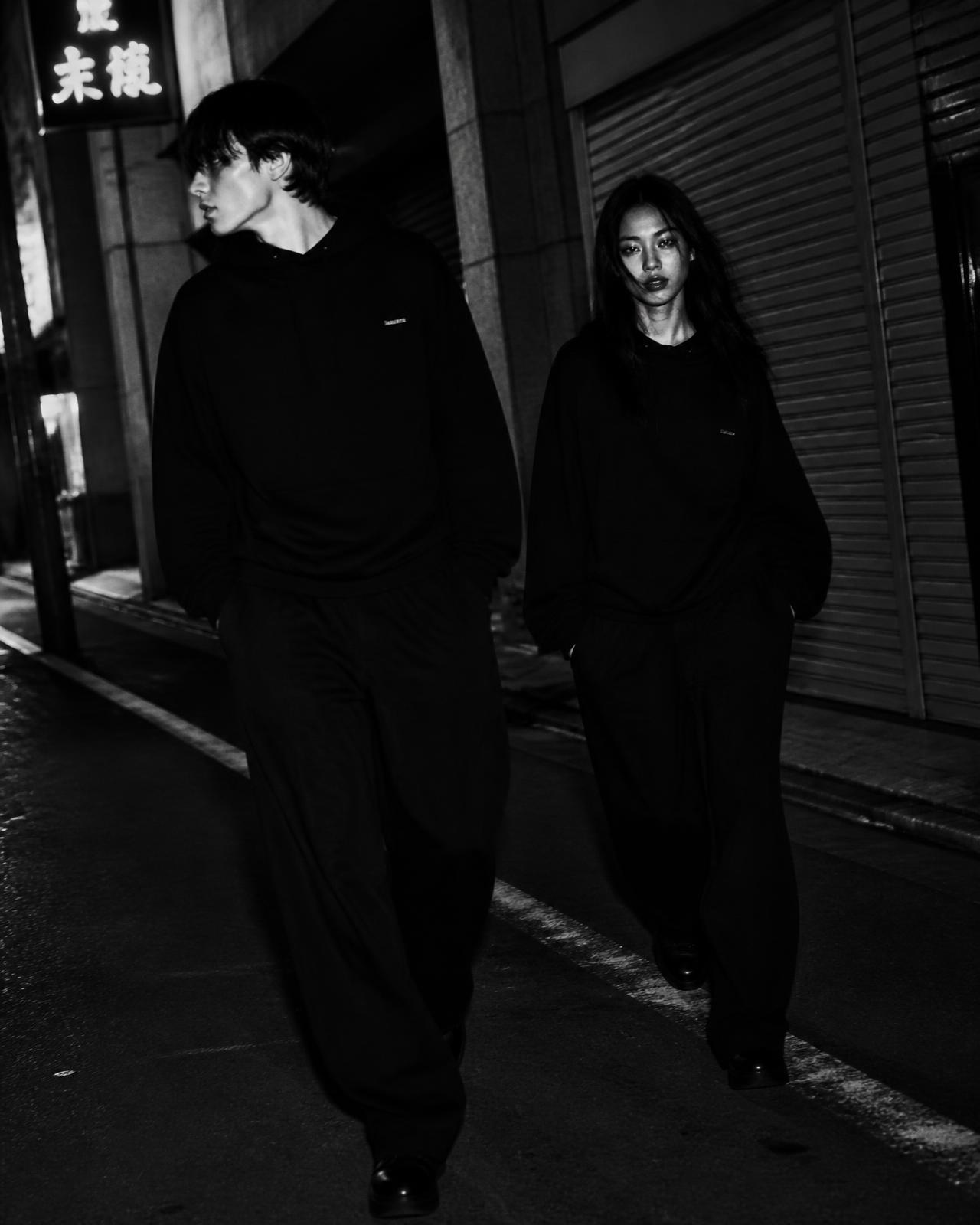 Two models in monochrome streetwear walking an urban alley at night